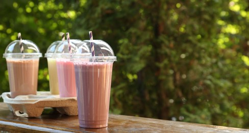 Photo of Tasty milkshakes in plastic cups on wooden table outdoors, space for text
