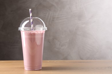 Photo of Tasty milkshake in plastic cup on wooden table, space for text