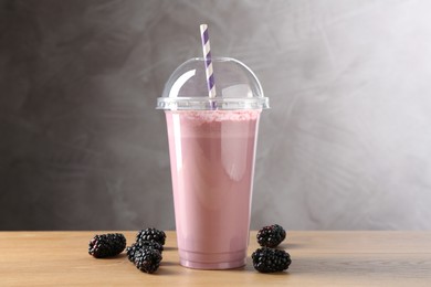 Photo of Tasty milkshake in plastic cup and blackberries on wooden table