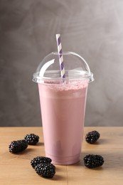 Photo of Tasty milkshake in plastic cup and blackberries on wooden table