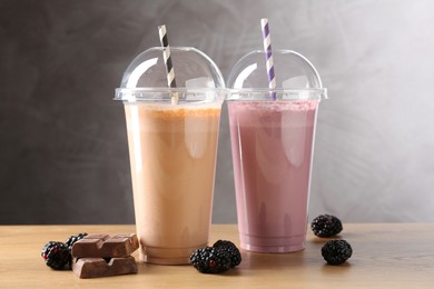 Photo of Tasty milkshakes in plastic cups and ingredients on wooden table