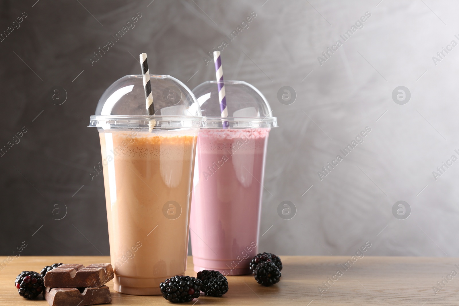 Tasty milkshakes in plastic cups and ingredients on wooden table, space for text Photo of Tasty milkshakes in plastic cups and ingredients on wooden table, space for text