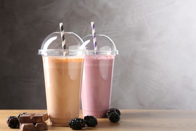 Photo of Tasty milkshakes in plastic cups and ingredients on wooden table, space for text