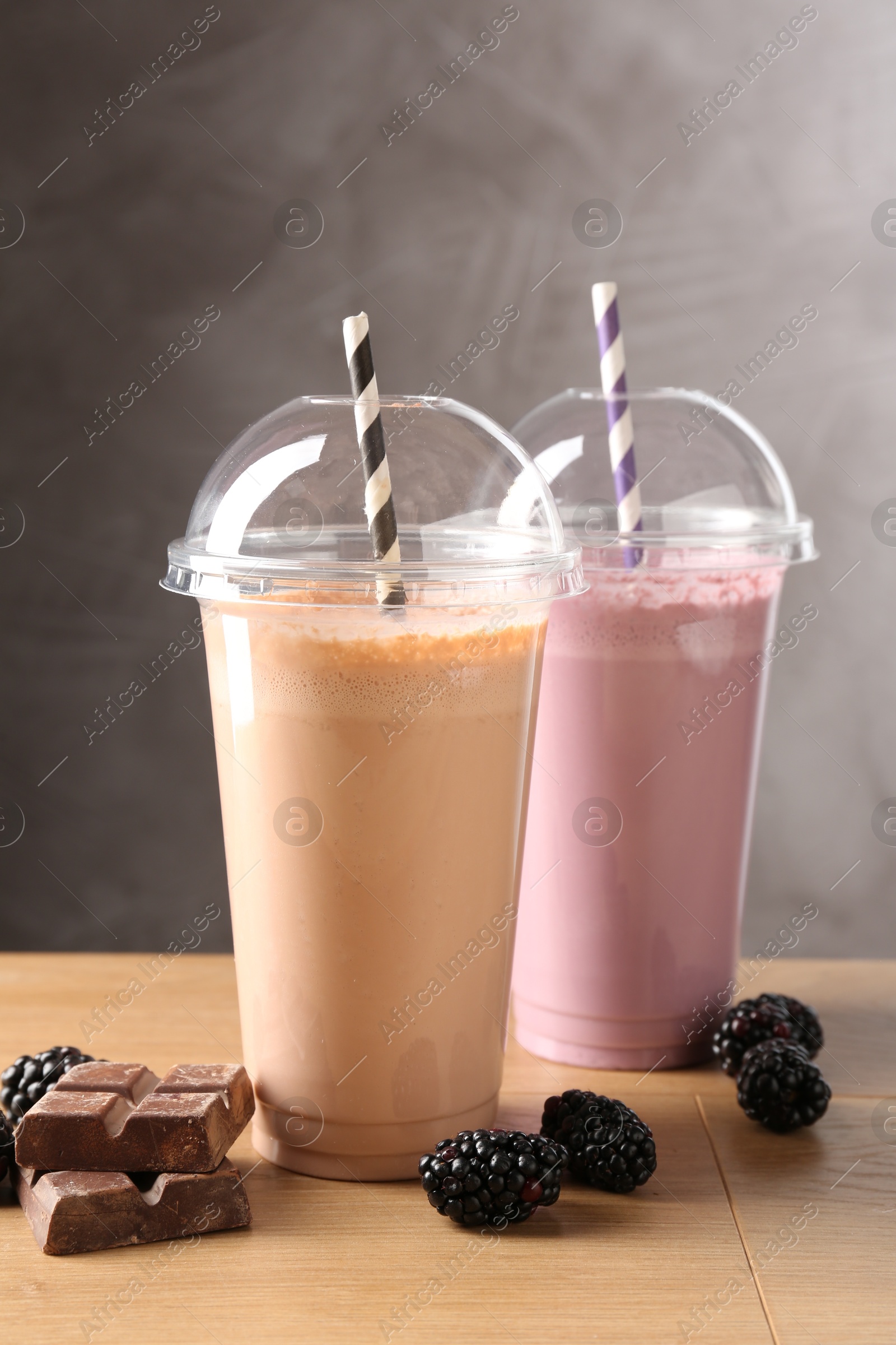 Tasty milkshakes in plastic cups and ingredients on wooden table Photo of Tasty milkshakes in plastic cups and ingredients on wooden table