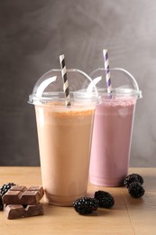 Photo of Tasty milkshakes in plastic cups and ingredients on wooden table