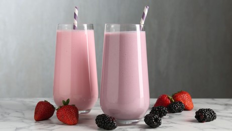 Photo of Tasty milkshakes in glasses and berries on white marble table