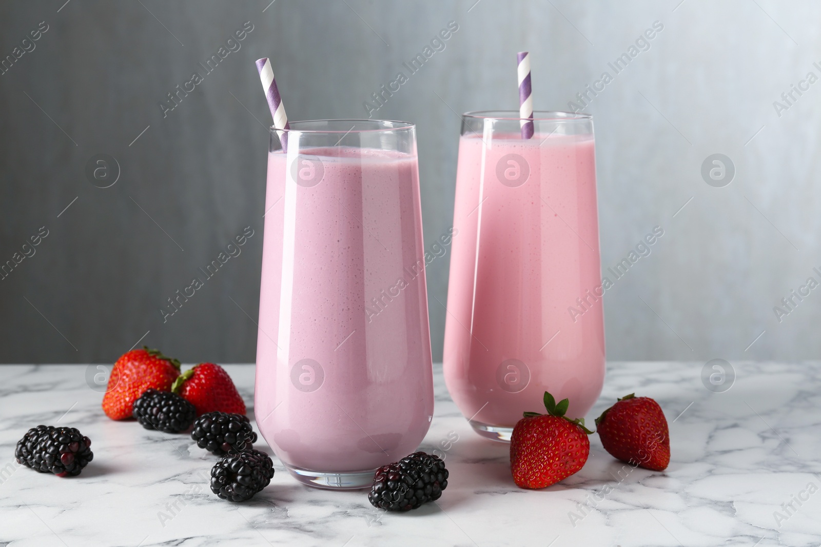Tasty milkshakes in glasses and berries on white marble table Photo of Tasty milkshakes in glasses and berries on white marble table