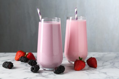 Photo of Tasty milkshakes in glasses and berries on white marble table