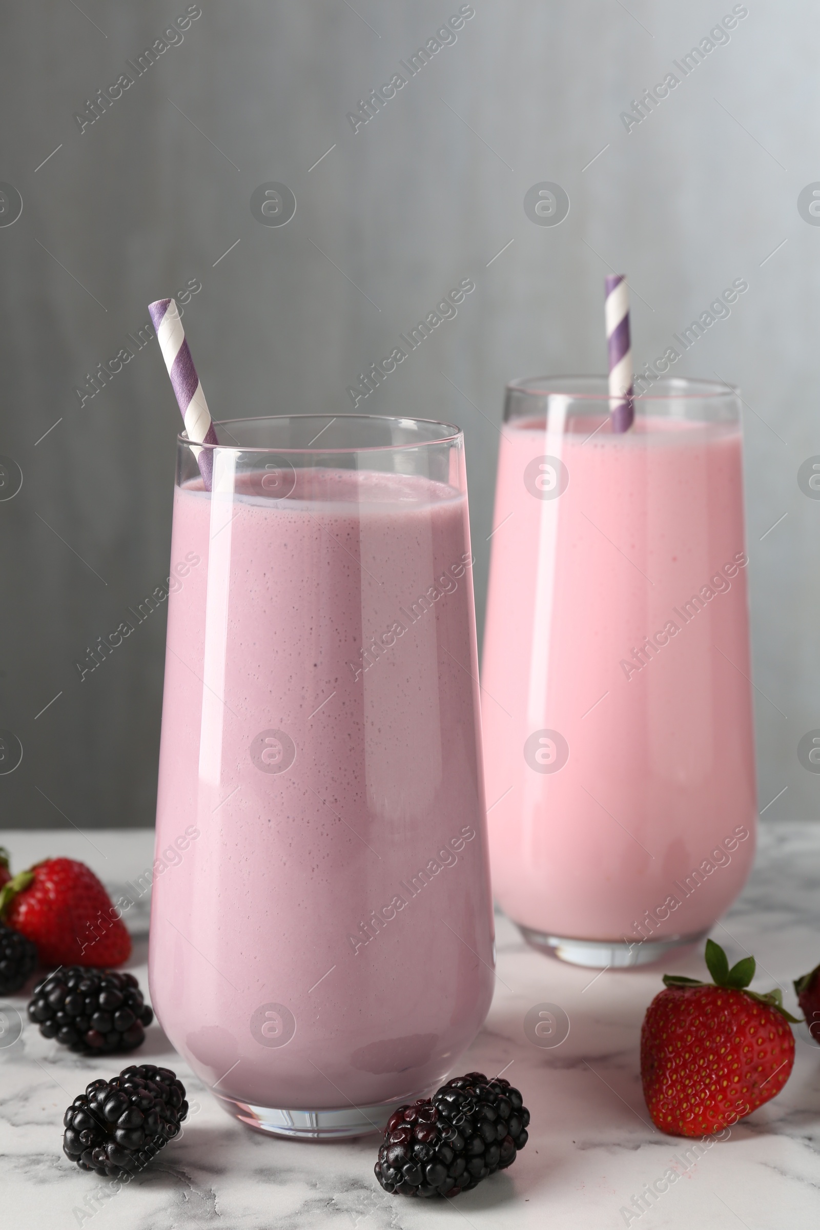 Tasty milkshakes in glasses and berries on white marble table Photo of Tasty milkshakes in glasses and berries on white marble table