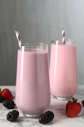 Photo of Tasty milkshakes in glasses and berries on white marble table