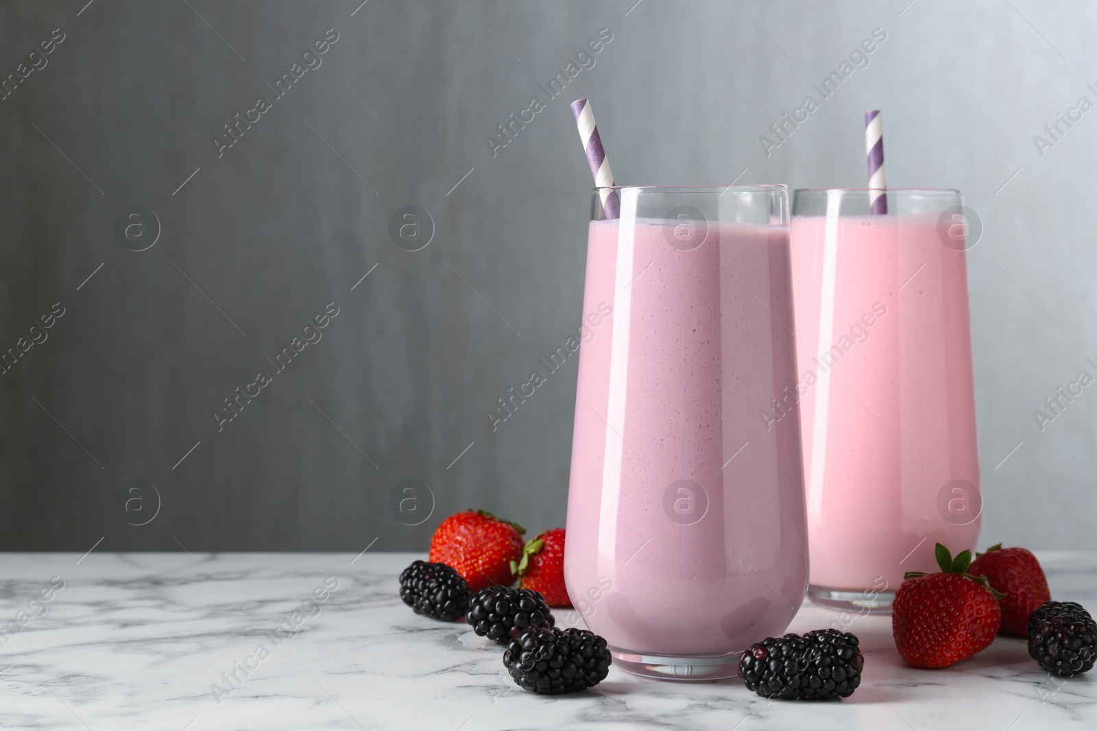 Photo of Tasty milkshakes in glasses and berries on white marble table, space for text