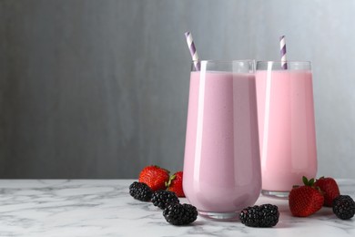 Photo of Tasty milkshakes in glasses and berries on white marble table, space for text