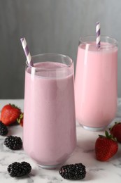Photo of Tasty milkshakes in glasses and berries on white marble table, closeup