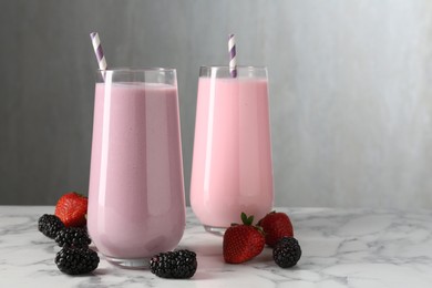 Photo of Tasty milkshakes in glasses and berries on white marble table, space for text