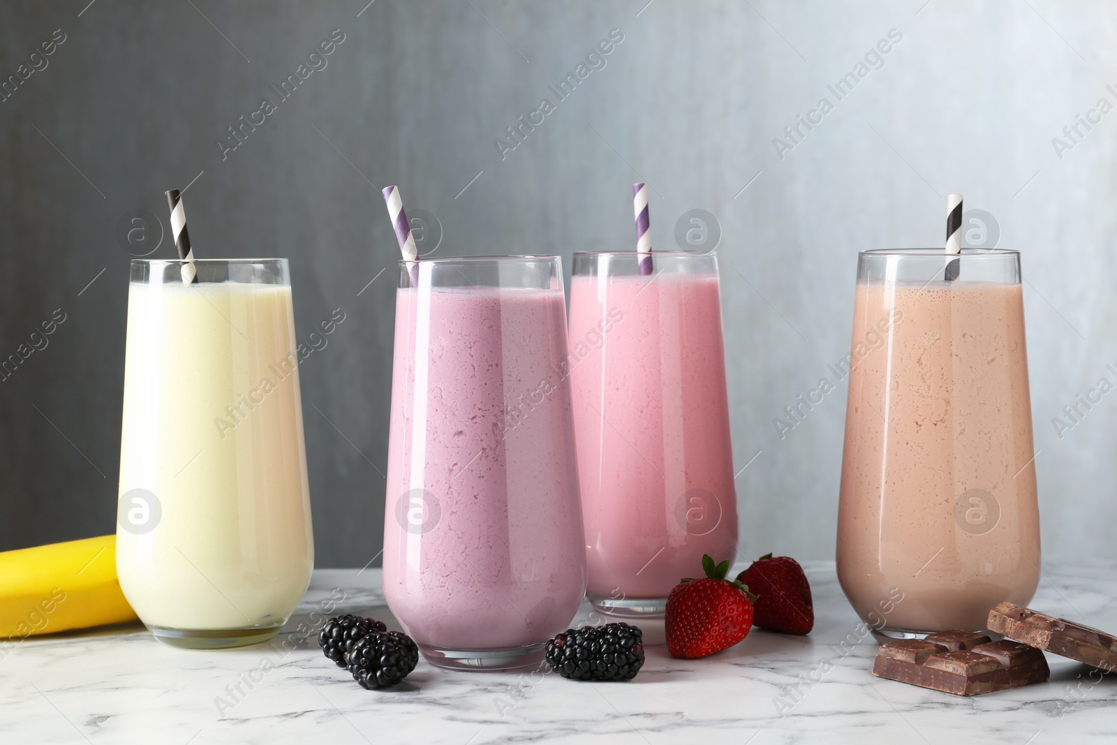 Tasty milkshakes in glasses and ingredients on white marble table Photo of Tasty milkshakes in glasses and ingredients on white marble table