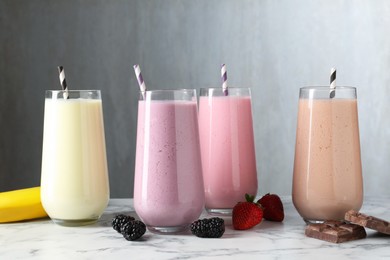 Photo of Tasty milkshakes in glasses and ingredients on white marble table