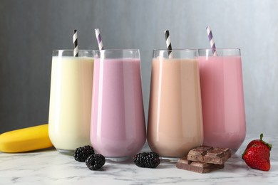 Photo of Tasty milkshakes in glasses and ingredients on white marble table
