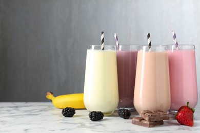 Photo of Tasty milkshakes in glasses and ingredients on white marble table, space for text