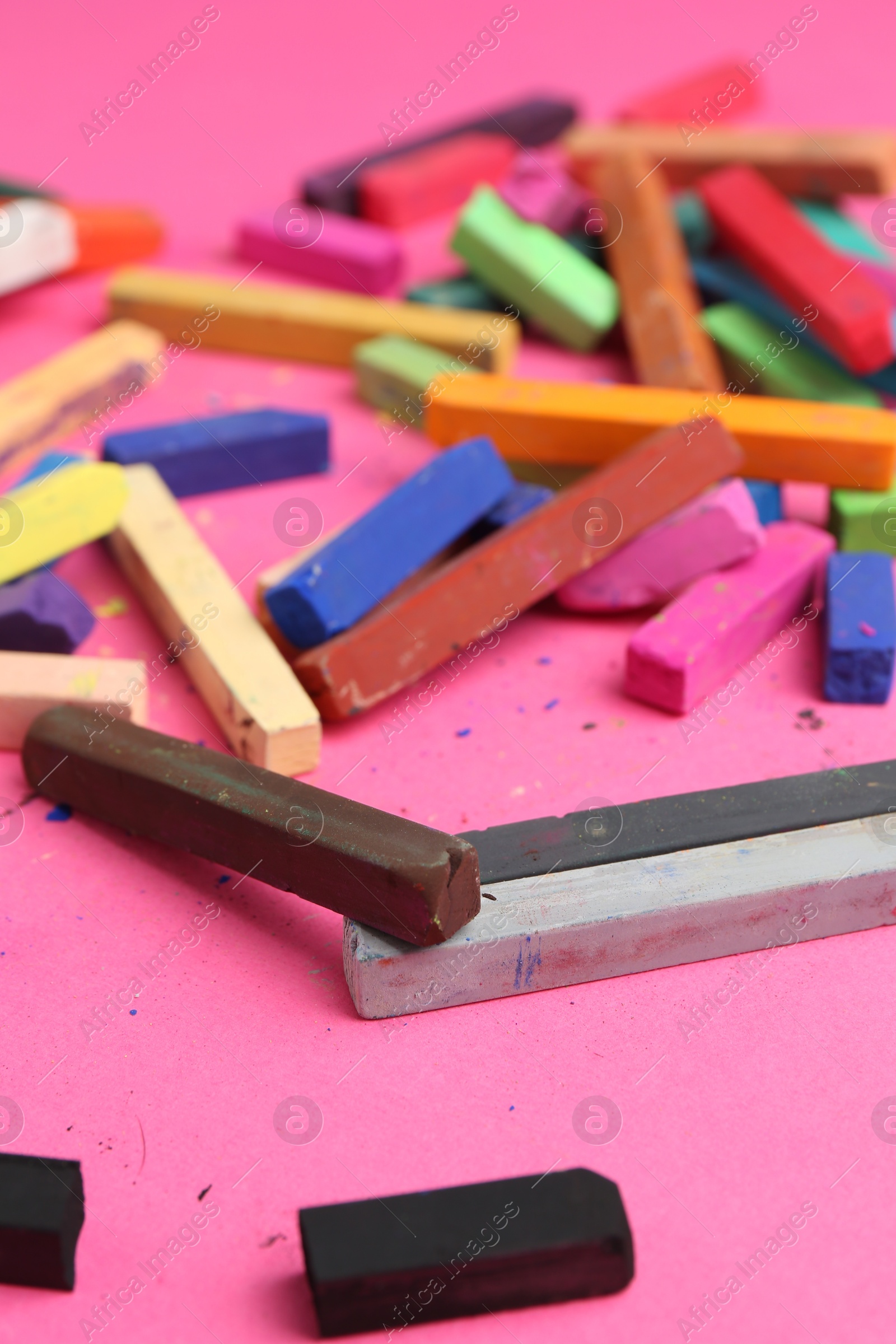 Photo of Many colorful chalk pastels on pink background, closeup