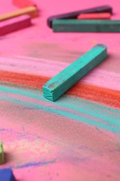 Photo of Many colorful chalk pastels on pink background, closeup
