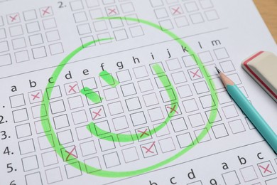Photo of Answer sheet with drawn happy face, pencil and eraser on table, closeup. Student passing exam