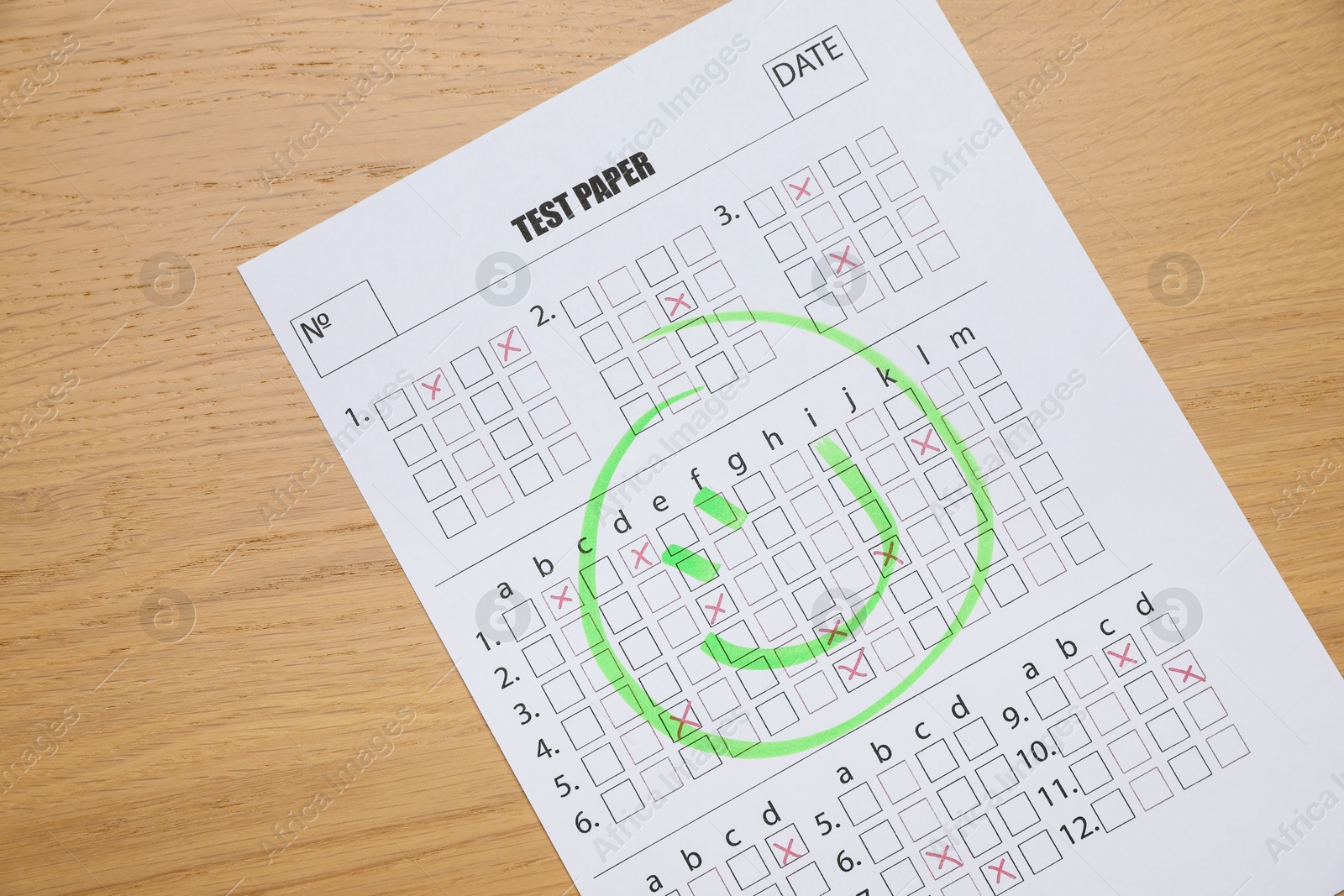 Photo of Answer sheet with drawn happy face on wooden table, top view. Student passing exam
