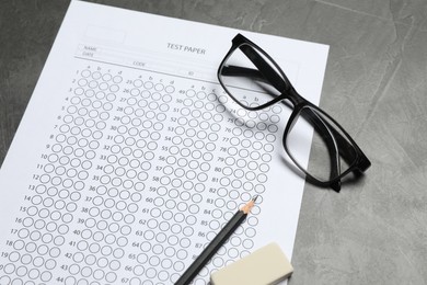 Photo of Answer sheet, glasses, pencil and eraser on gray textured table, closeup. Student passing exam