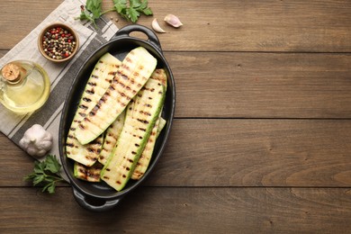 Photo of Delicious grilled courgette slices in baking dish, oil and spices on wooden table, flat lay. Space for text