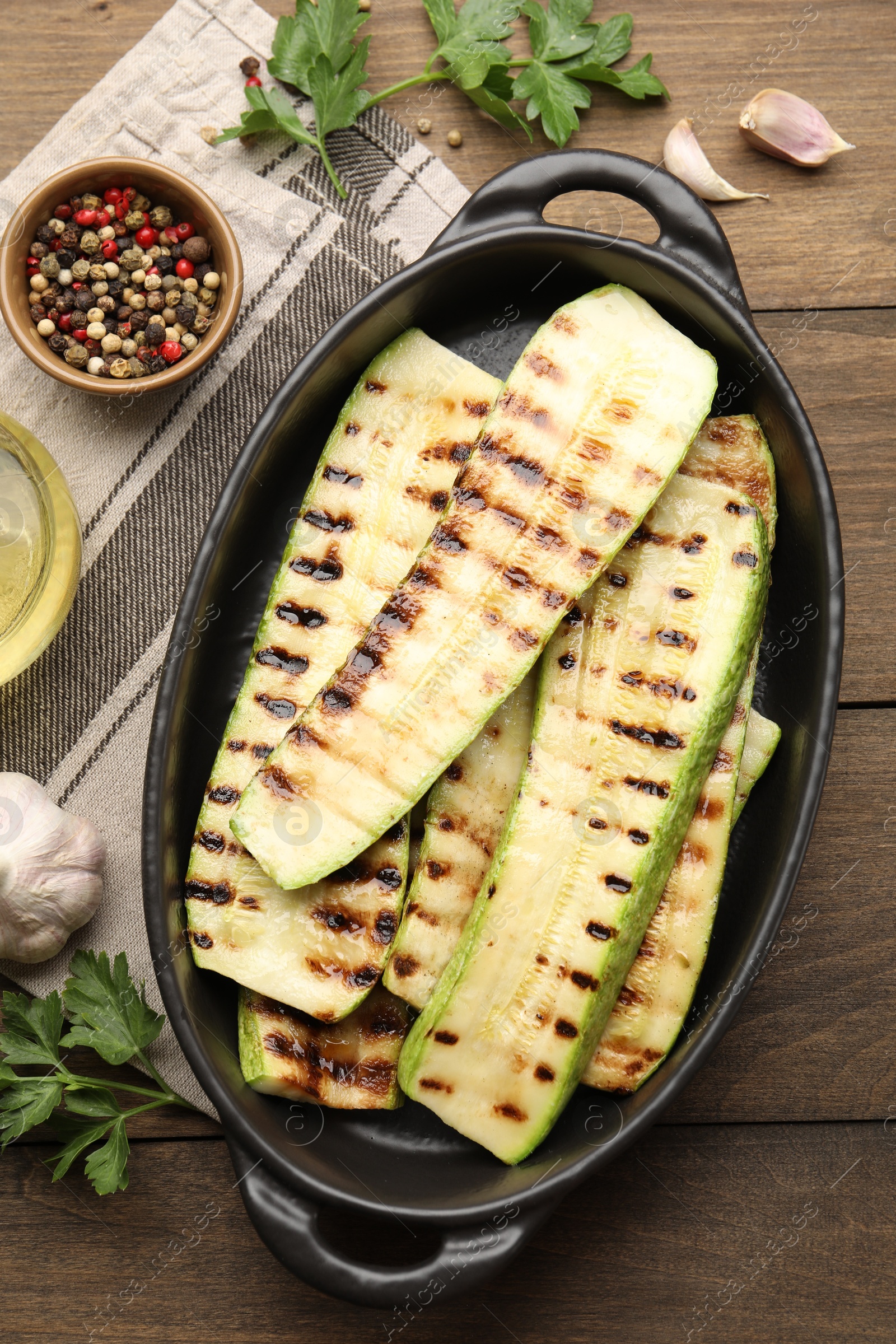 Photo of Delicious grilled courgette slices in baking dish and spices on wooden table, flat lay