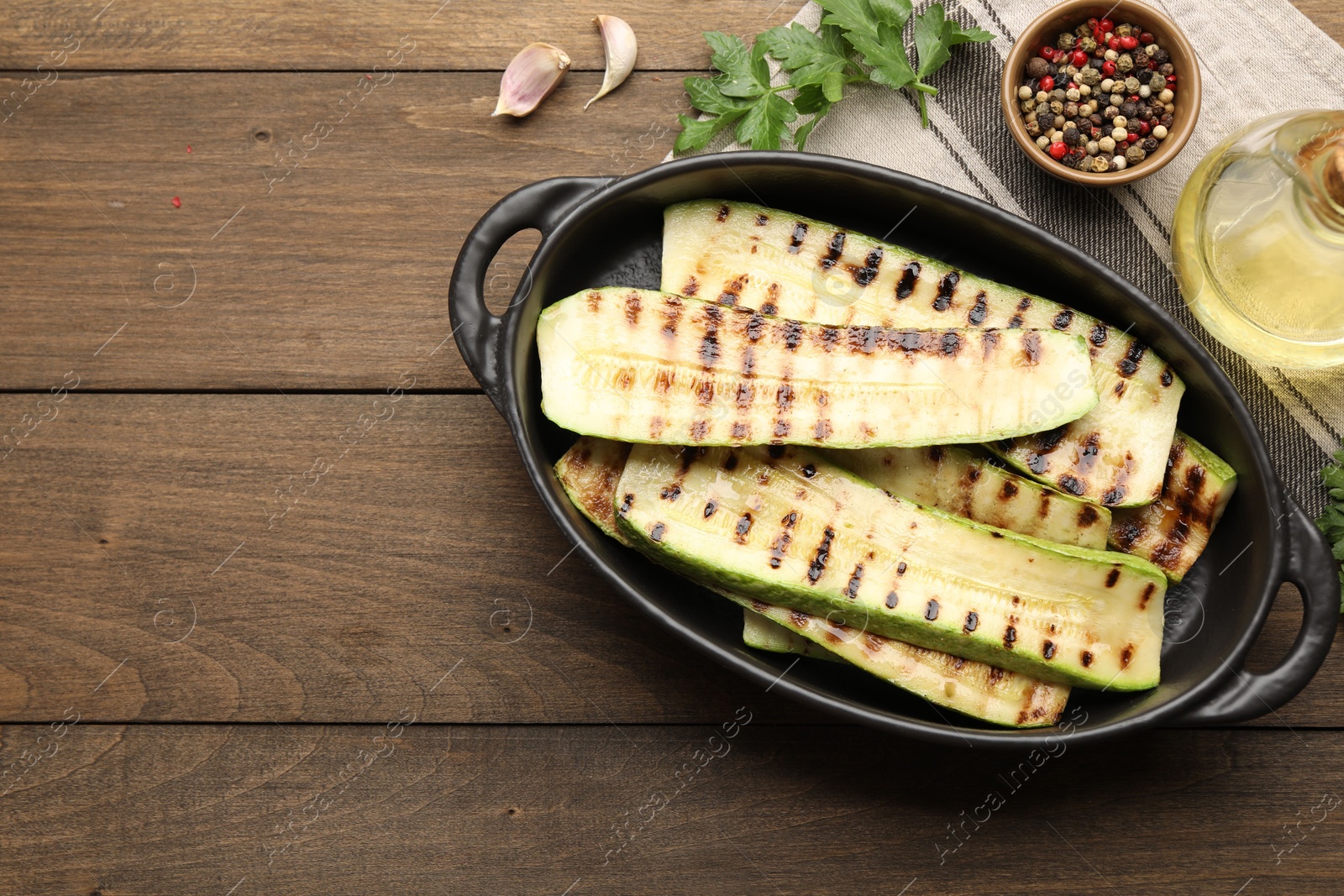 Photo of Delicious grilled courgette slices in baking dish, oil and spices on wooden table, flat lay. Space for text