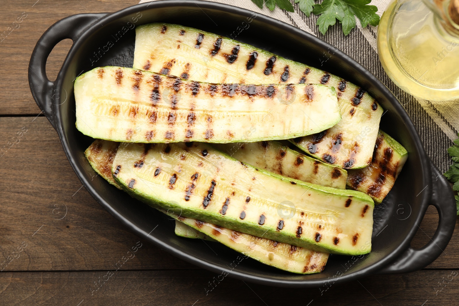 Photo of Delicious grilled courgette slices in baking dish, oil and parsley on wooden table, flat lay