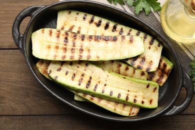 Photo of Delicious grilled courgette slices in baking dish, oil and parsley on wooden table, flat lay