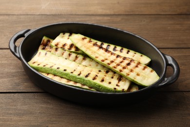 Photo of Delicious grilled courgette slices in baking dish on wooden table, closeup