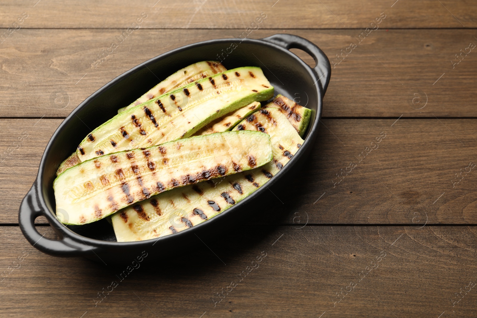 Photo of Delicious grilled courgette slices in baking dish on wooden table, above view