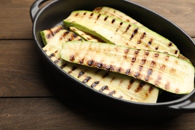 Photo of Delicious grilled courgette slices in baking dish on wooden table, closeup
