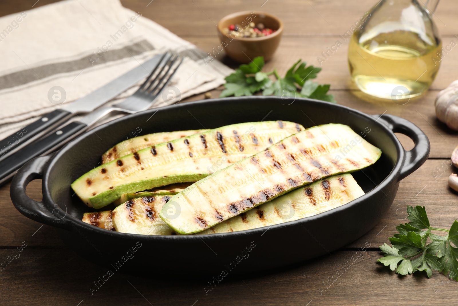 Photo of Delicious grilled courgette slices in baking dish and parsley on wooden table, closeup