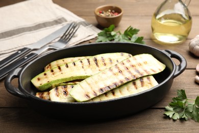 Photo of Delicious grilled courgette slices in baking dish and parsley on wooden table, closeup