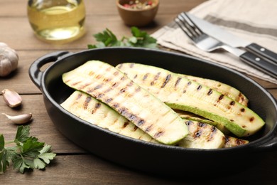 Photo of Delicious grilled courgette slices in baking dish and parsley on wooden table, closeup