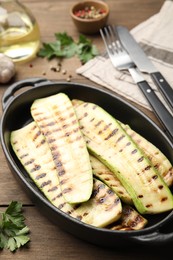 Photo of Delicious grilled courgette slices in baking dish and parsley on wooden table, closeup