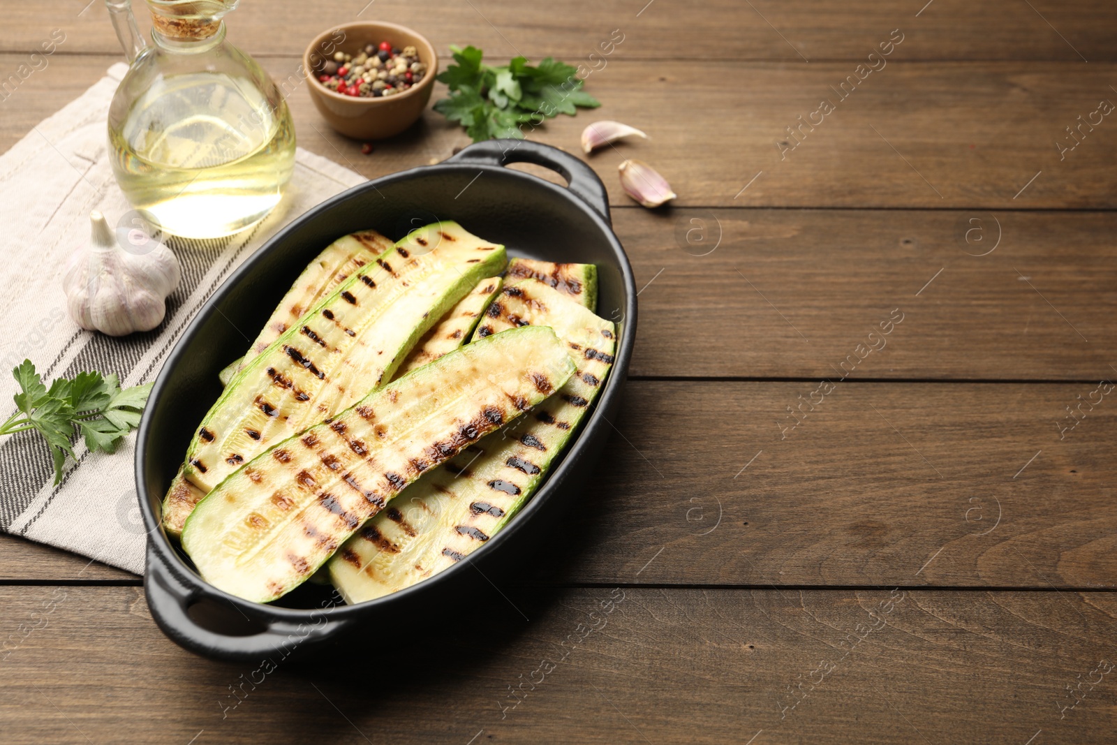 Photo of Delicious grilled courgette slices in baking dish, spices and parsley on wooden table, space for text