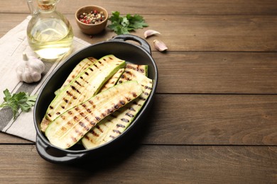 Photo of Delicious grilled courgette slices in baking dish, spices and parsley on wooden table, space for text
