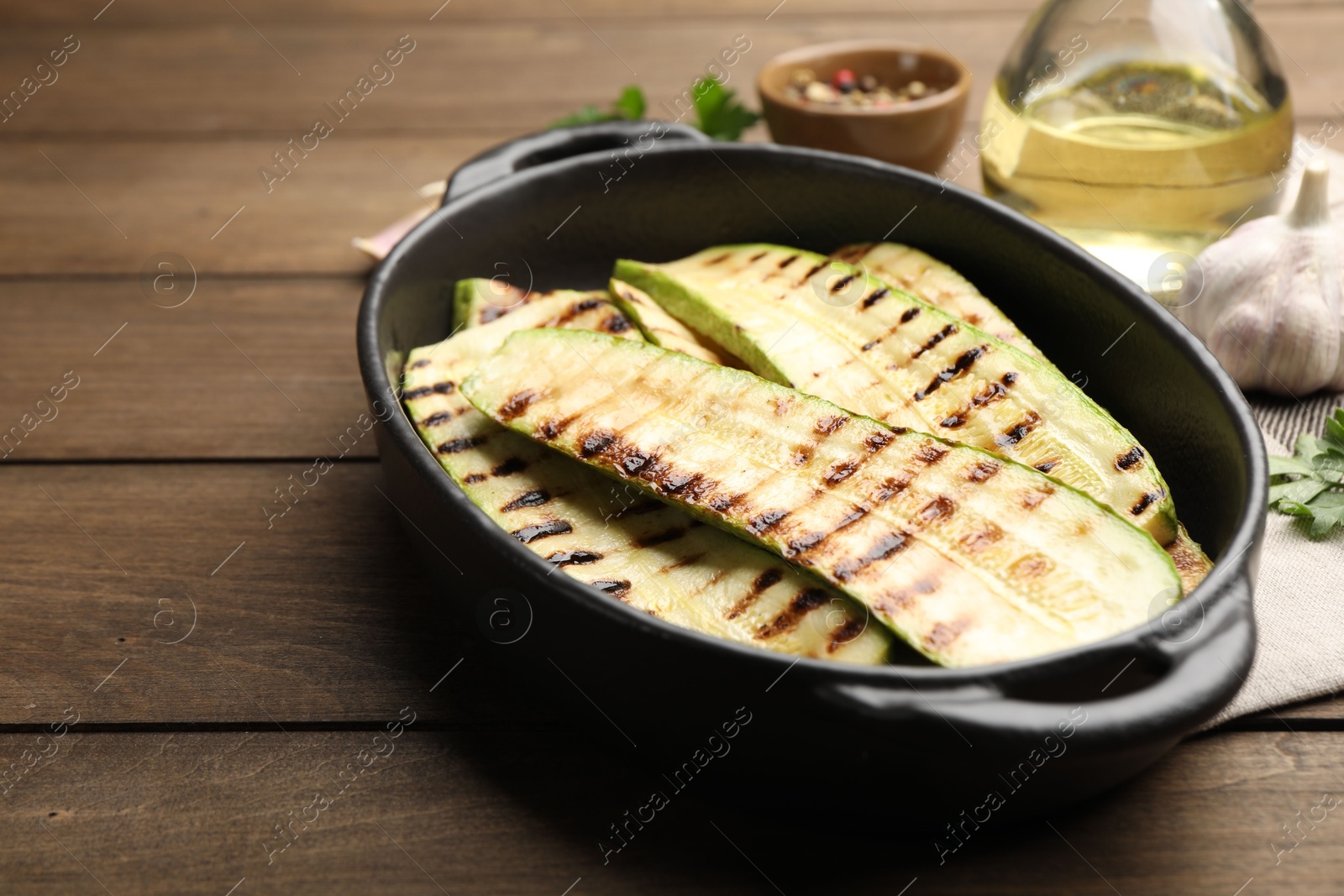 Photo of Delicious grilled courgette slices in baking dish on wooden table, closeup