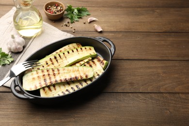 Photo of Delicious grilled courgette slices in baking dish, spices and parsley on wooden table, space for text