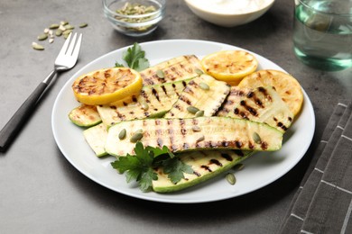 Photo of Delicious grilled courgette slices with pumpkin seeds, lemon and parsley on grey table, closeup