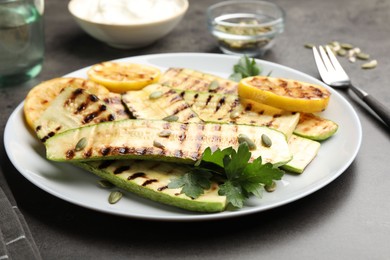 Photo of Delicious grilled courgette slices with pumpkin seeds, lemon and parsley on grey table, closeup