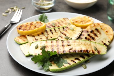 Photo of Delicious grilled courgette slices with pumpkin seeds, lemon and parsley on grey table, closeup