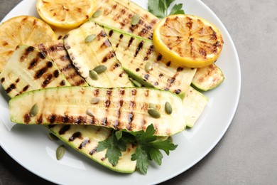 Photo of Delicious grilled courgette slices with pumpkin seeds, lemon and parsley on grey table, above view