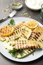Photo of Delicious grilled courgette slices with pumpkin seeds, lemon and parsley on grey table, closeup