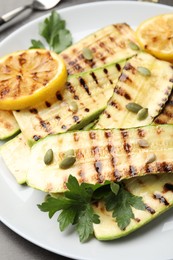 Photo of Delicious grilled courgette slices with pumpkin seeds, lemon and parsley on grey table, closeup