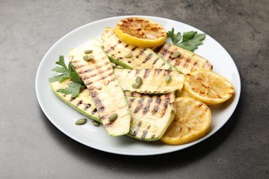 Photo of Delicious grilled courgette slices with pumpkin seeds, lemon and parsley on grey table, closeup